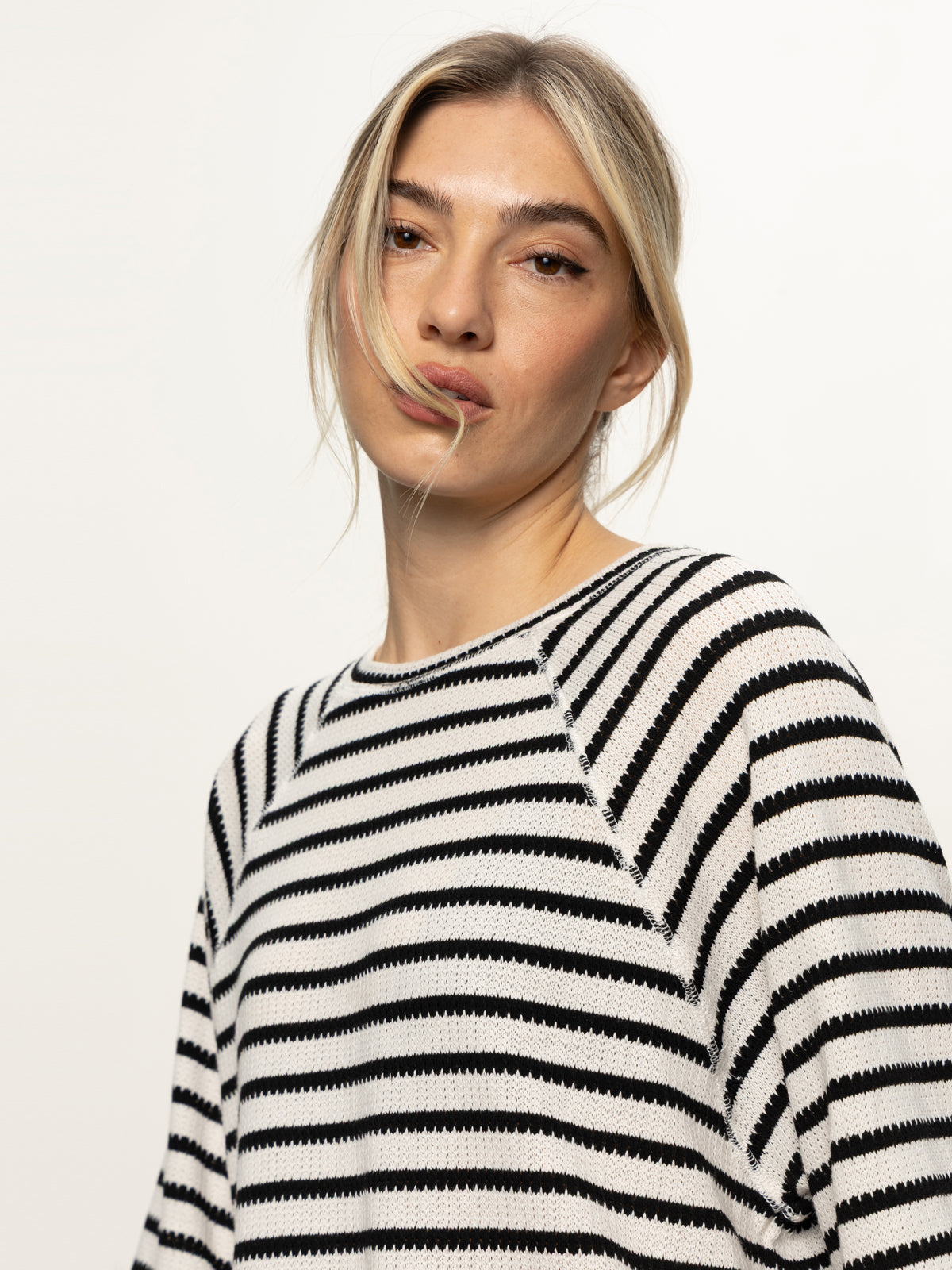 A woman with blonde hair wears the Sanctuary Clothing boxy raglan tee in black with light oat stripe, looking at the camera against a plain, light background.