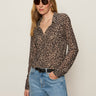 A woman wearing the Sanctuary Clothing dreamers top french kitty, sunglasses, and light blue jeans stands against a plain light background with one hand in her pocket.