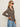 Woman in sunglasses and gold earrings wears the Sanctuary Clothing "dreamers top french kitty," a long-sleeve leopard print blouse with blue jeans, posing in profile against a plain, light background.
