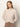 A woman with straight, light brown hair models the Sanctuary Clothing long sleeve draped mock neck top in mother of pearl, posing with hands behind her back against a plain light background.