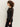 A person with curly hair stands in profile against a plain light background, wearing the Sanctuary Clothing sparkle mesh crew tee black and black pants.