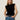 A woman with long blonde hair wears the Sanctuary Clothing pleated sleeveless top in black and blue jeans, accessorized with a black belt, standing against a neutral background with a relaxed expression.