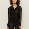 A woman with curly hair wears the Sanctuary Clothing dreamland ruffle top in black and pinstriped black pants, standing against a plain light background.