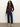 A woman with curly hair wears the Sanctuary Clothing fitted mesh button down top boheme in maroon, paired with blue cropped jeans and beige boots, standing against a plain light background.