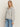 A woman with long blonde hair wears the Sanctuary Clothing textured zip up popover in heather grey and blue jeans, standing against an off-white background and looking slightly to the side.