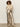 A woman with curly hair wears the Sanctuary Clothing ruffle lace tee in vintage ivory, paired with metallic gold high-waisted wide-leg pants, a beige belt, and beige pointed-toe boots against a plain light wall.