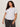 A woman with long curly hair models the Sanctuary Clothing embellished tee in white (extended sizing) and dark gray jeans, standing against a plain light-colored background.