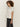 A person with curly hair stands sideways against an off-white background, wearing the Sanctuary Clothing embellished tee white and dark wide-leg jeans.
