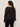 A woman with curly hair faces away, wearing Sanctuary Clothing's lovely lace button front top in black extended sizing with black pants, set against a plain light background.