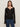 A woman with long brown hair wears the Sanctuary Clothing lovely lace button front top in black and blue jeans, standing facing forward against a plain light-colored background.