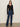 A woman stands against a plain background wearing the Sanctuary Clothing lovely lace button front top in black, paired with high-waisted blue jeans, a black belt, and black shoes. She has straight brown hair and earrings.