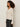A woman with curly hair wears the Sanctuary Clothing lovely lace button front top in vintage ivory and black jeans, standing in profile against a plain light background.