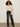 A woman with curly hair and black sunglasses wears the Sanctuary Clothing lovely lace button front top in vintage ivory, a black belt, dark high-waisted wide-leg jeans, and black heeled boots against a plain background.