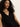 A woman with long curly hair wears the sleeveless black "Relaxed Modern Vest" by Sanctuary Clothing, standing against a light background. She has a neutral expression and is slightly leaning.