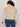A person with curly dark hair and sunglasses is shown from the back against a plain background, wearing Sanctuary Clothing's silky fur vest almond cream (extended sizing) over a white long-sleeve top and blue jeans.