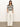 A person with long hair stands against a plain wall, wearing Sanctuary Clothing's knitted collared top in black and chalk. They have their hands in their pockets and face forward, completing the look with wide-leg white pinstriped pants.