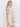 A woman with wavy blonde hair models the Sanctuary Clothing summer shell dress eco natural, a sleeveless cream crochet style, standing sideways against a white background.