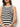 A woman in a Sanctuary Clothing "summer shell dress" featuring chalk black stripes stands against a plain background, gently resting her hands in front. She wears hoop earrings, has long brown hair, and her face is partially out of frame.