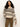 A woman with curly dark hair wears the Sanctuary Clothing fairisle crew neck sweater in light oat multi and brown corduroy pants, standing against a plain off-white background.