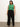 Person standing against a plain background wearing a green sleeveless top and black wide