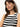 A woman with long brown hair and hoop earrings wears a Sanctuary Clothing crochet shell sweater in chalk black stripe and a gold chain necklace. She stands against a plain white background, looking slightly towards the camera.