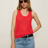 A woman wearing dark sunglasses, Sanctuary Clothing's mesh stitch shell sweater in cayenne, and light blue jeans with a black belt stands against a plain light background, one hand on her hip.