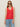 A woman in the Sanctuary Clothing mesh stitch shell sweater in cayenne, sunglasses, and light blue jeans stands against a beige background. She has long straight hair and a neutral expression.