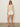 A woman wearing the Sanctuary Clothing mesh stitch shell sweater macrame stands against a plain light background, looking relaxed with sunglasses, white shorts, and beige slide sandals”one hand by her side.