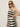 A woman wearing dark sunglasses and the Sanctuary Clothing mesh stitch shell sweater in black chalk stripe stands against a plain, light-colored wall with one hand on her hip, looking confidently at the camera.