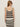 A woman with long, light brown hair, sunglasses, and hoop earrings faces away, wearing the Sanctuary Clothing mesh stitch shell sweater in black chalk stripe against a plain light background.