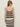 A woman with long, light brown hair, sunglasses, and hoop earrings faces away, wearing the Sanctuary Clothing mesh stitch shell sweater in black chalk stripe against a plain light background.