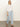 A woman with straight blonde hair and a neutral expression wears the Sanctuary Clothing easy knitwear top in white, paired with light blue wide-leg pants and brown sandals, standing against a plain background.