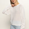 A woman with straight blonde hair models the Sanctuary Clothing easy knitwear top in white and light blue jeans, standing against a plain background with her left hand touching her neck.