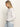 A woman with long blonde hair wears the Sanctuary Clothing easy knitwear top in white and light blue jeans, standing in profile with hands in her pockets against a plain light background.
