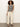 A woman with curly hair wears the Sanctuary Clothing modern sweater shell in black macrame, styled with wide-leg cream pants and black strappy sandals, as she stands against a plain white wall.