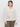 A person in a chalk open knit bomber jacket by Sanctuary Clothing stands against a white background. They have medium-length dark hair, are wearing hoop earrings, and maintain a neutral expression.