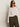 A woman in Sanctuary Clothing's textured raglan crew in white light oat stripe (extended sizing) and high-waisted olive green pants stands against a plain light-colored background.