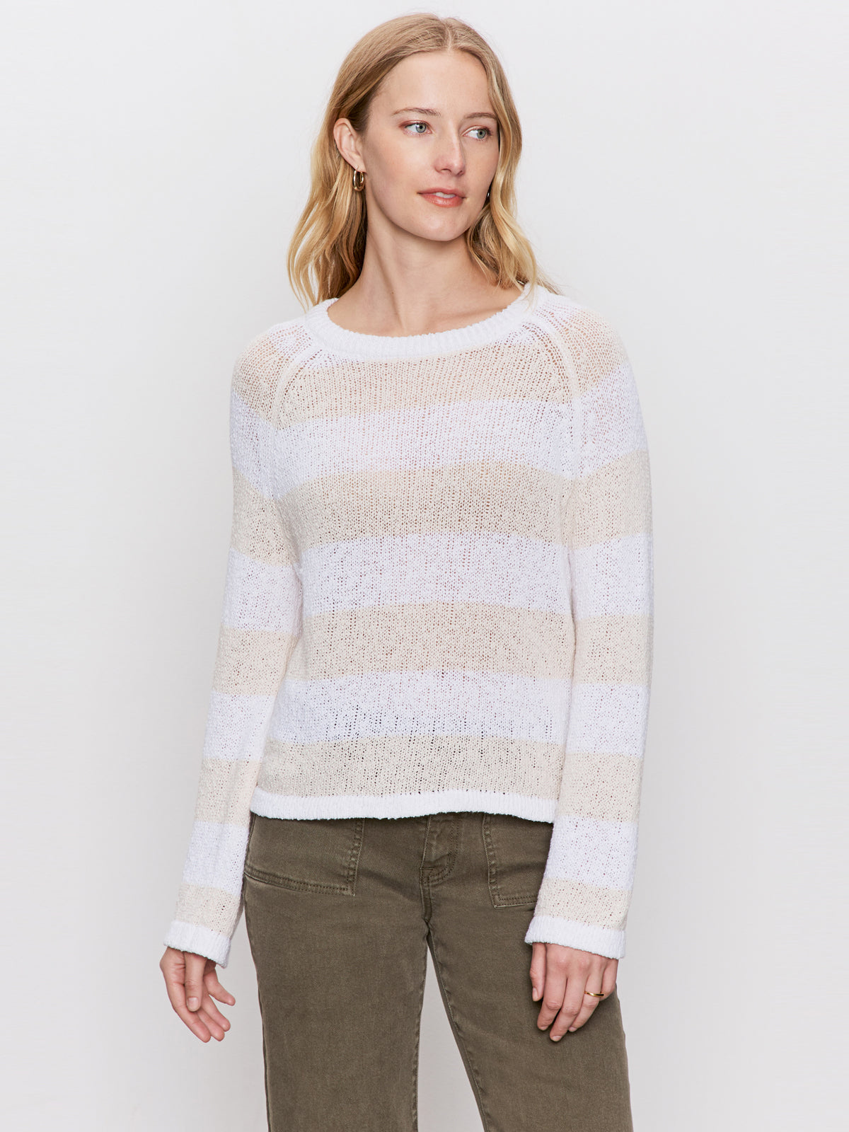A woman with long blonde hair models the Sanctuary Clothing textured raglan crew in white light oat stripe, paired with olive green pants, against a plain light background.