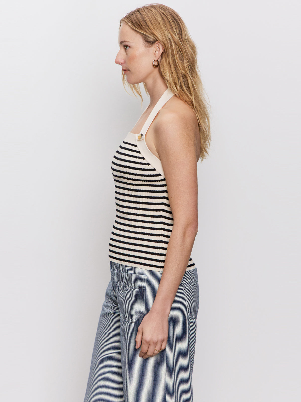 A woman with wavy blonde hair stands in profile against a white background, wearing the Sanctuary Clothing sunkissed rib halter top in black macrame stripe.