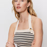 A woman with long blonde hair wears the Sanctuary Clothing sunkissed rib halter top in black macrame stripe, paired with gold hoop earrings and a gold ring, standing against a plain white background with her arms crossed.