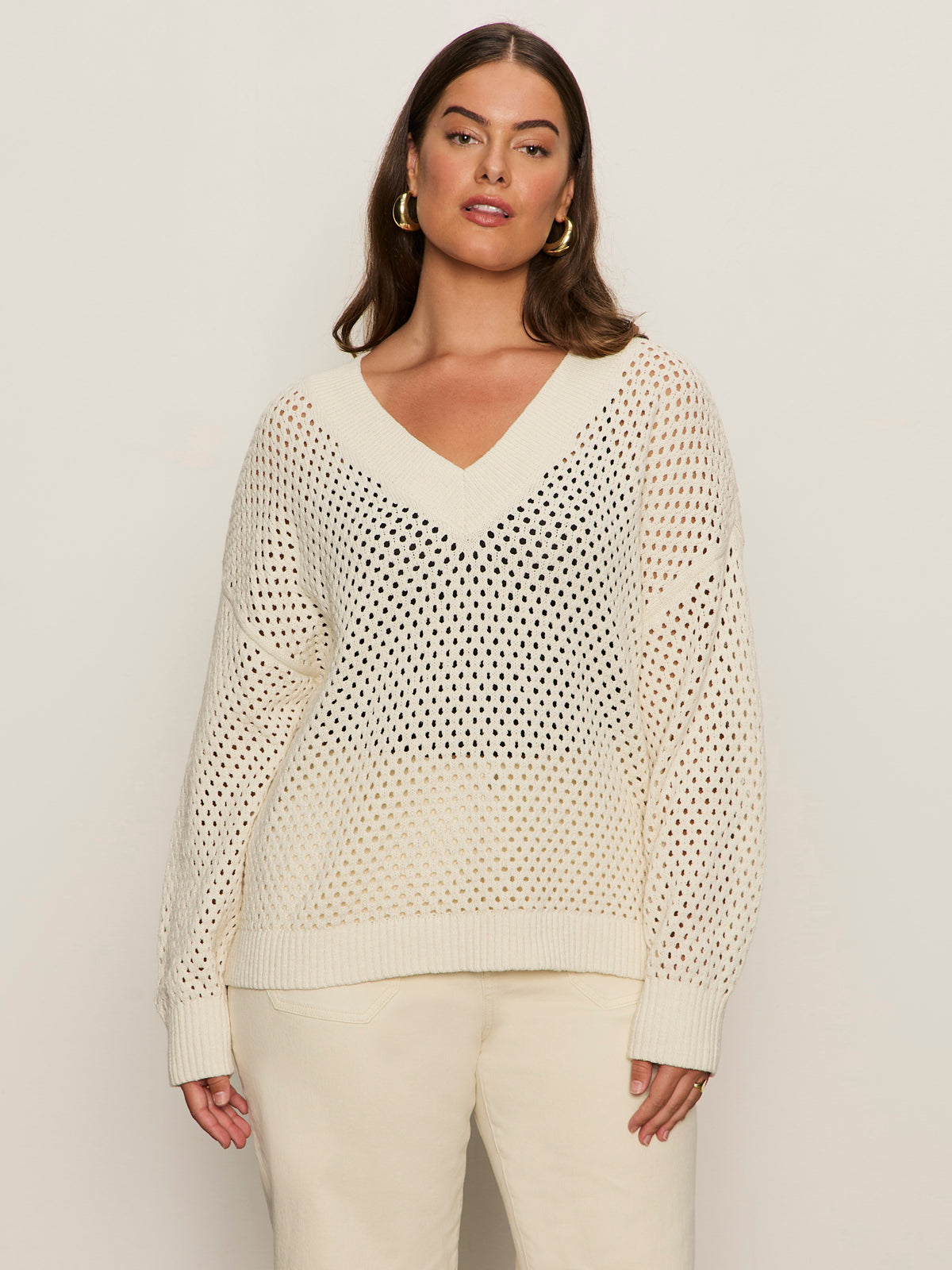 A woman with long brown hair wears the Sanctuary Clothing airy openwork sweater macrame (extended sizing) in cream with matching pants, standing against a plain light background.