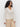 A woman with curly hair wears the Sanctuary Clothing airy openwork sweater macrame in cream over light beige wide-leg pants, standing against a plain white background.