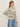 A woman with light brown hair and a neutral expression stands sideways against a plain background, wearing Sanctuary Clothing's airy openwork sweater in chalk black stripe, paired with light blue jeans and gold hoop earrings.