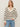 A woman with long blonde hair models the Sanctuary Clothing airy openwork sweater in chalk black stripe, paired with light blue jeans, standing against a plain light background.