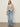 A woman stands against a plain background wearing the Sanctuary Clothing airy openwork sweater in chalk black stripe, paired with light blue high-waisted jeans, black heeled sandals, and gold earrings. Her left hand is in her pocket and she looks relaxed.
