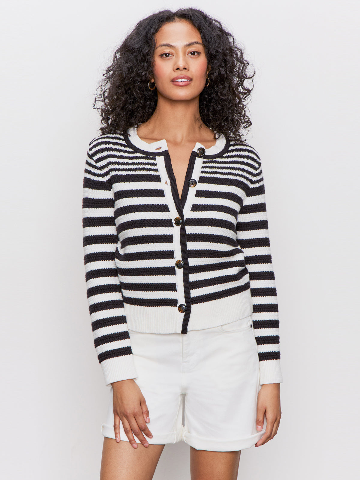 A woman with curly hair wears the Sanctuary Clothing city summer cardi in black macrame multi stripe over white shorts, standing against a plain white background.
