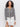 A woman with curly hair wears the Sanctuary Clothing city summer cardi in black macrame multi stripe over white shorts, standing against a plain white background.