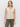 A woman with light brown hair models the Sanctuary Clothing textured sweater vest macrame—a sleeveless, cream knit design with buttons and two front pockets—paired with olive green pants against a white background.