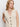 A woman with long, wavy blonde hair models the Sanctuary Clothing textured sweater vest macrame—a sleeveless, cream knit vest with black buttons and front pockets—against a plain white background, looking slightly to the side.
