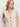 A woman with long, wavy blonde hair models the Sanctuary Clothing textured sweater vest macrame�a sleeveless, cream knit vest with black buttons and front pockets�against a plain white background, looking slightly to the side.